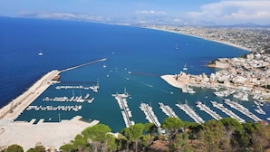 Una marina costera con numerosas embarcaciones amarradas, un muelle y un pueblo con edificios a lo largo de la costa.