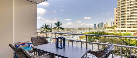 A balcony with wicker furniture, a table, and a view of a marina and buildings.
