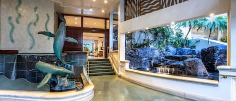 A lobby with a large aquarium, a staircase, and a view of a tropical garden.