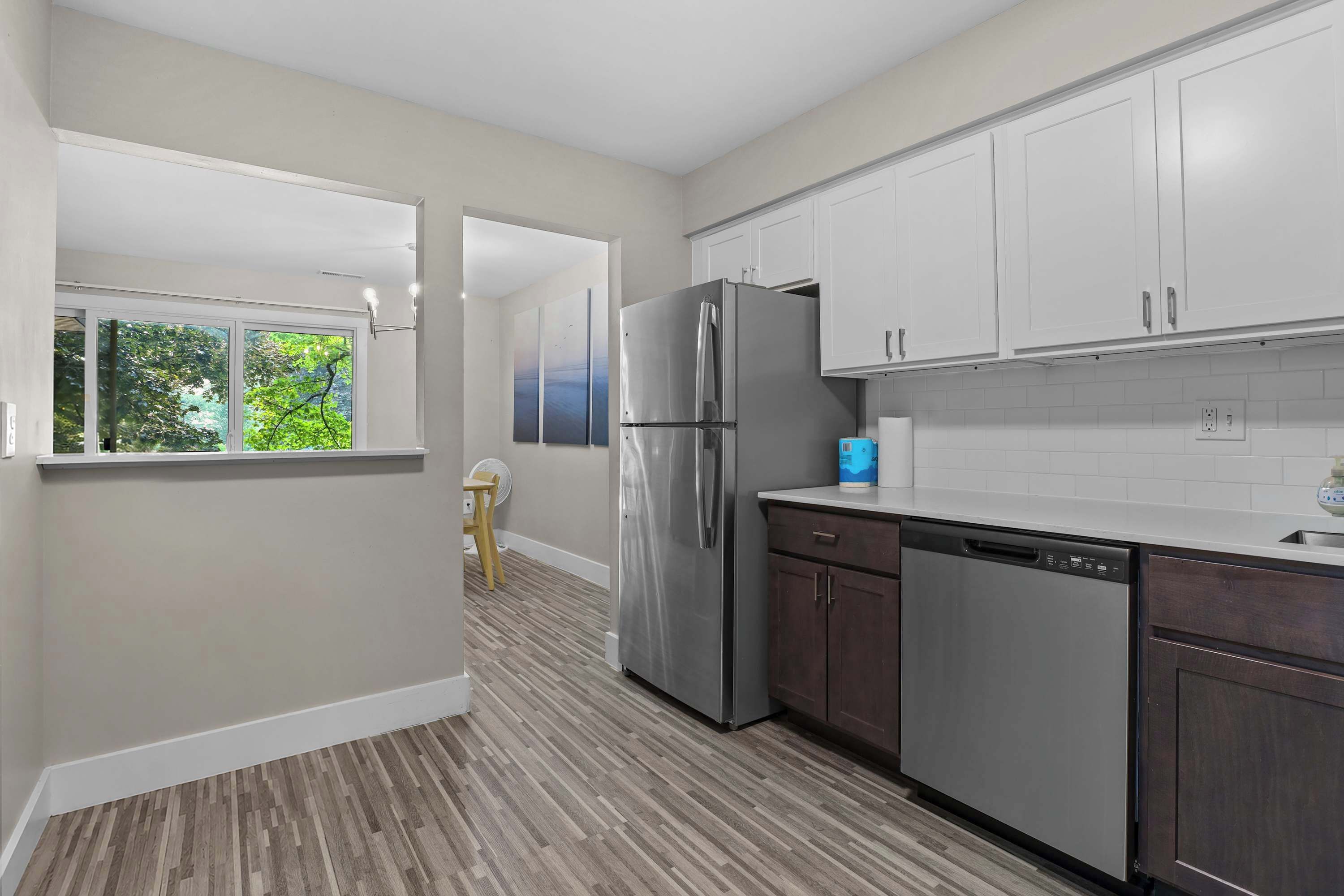 A modern kitchen with stainless steel appliances, white cabinetry, and a view through an open door to a room with a window overlooking greenery.