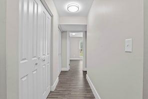 A hallway with white walls and wooden flooring leading to a door with a window. - Stunning Stay in Rochester Hills (Rochester Hills)