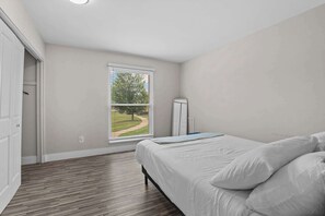 A bedroom with a bed, a window with blinds, a wardrobe, and a door leading to another room. - Stunning Stay in Rochester Hills (Rochester Hills)