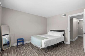A bedroom with a bed, a small blue chair, a mirror, and a door leading to another room. - Stunning Stay in Rochester Hills (Rochester Hills)
