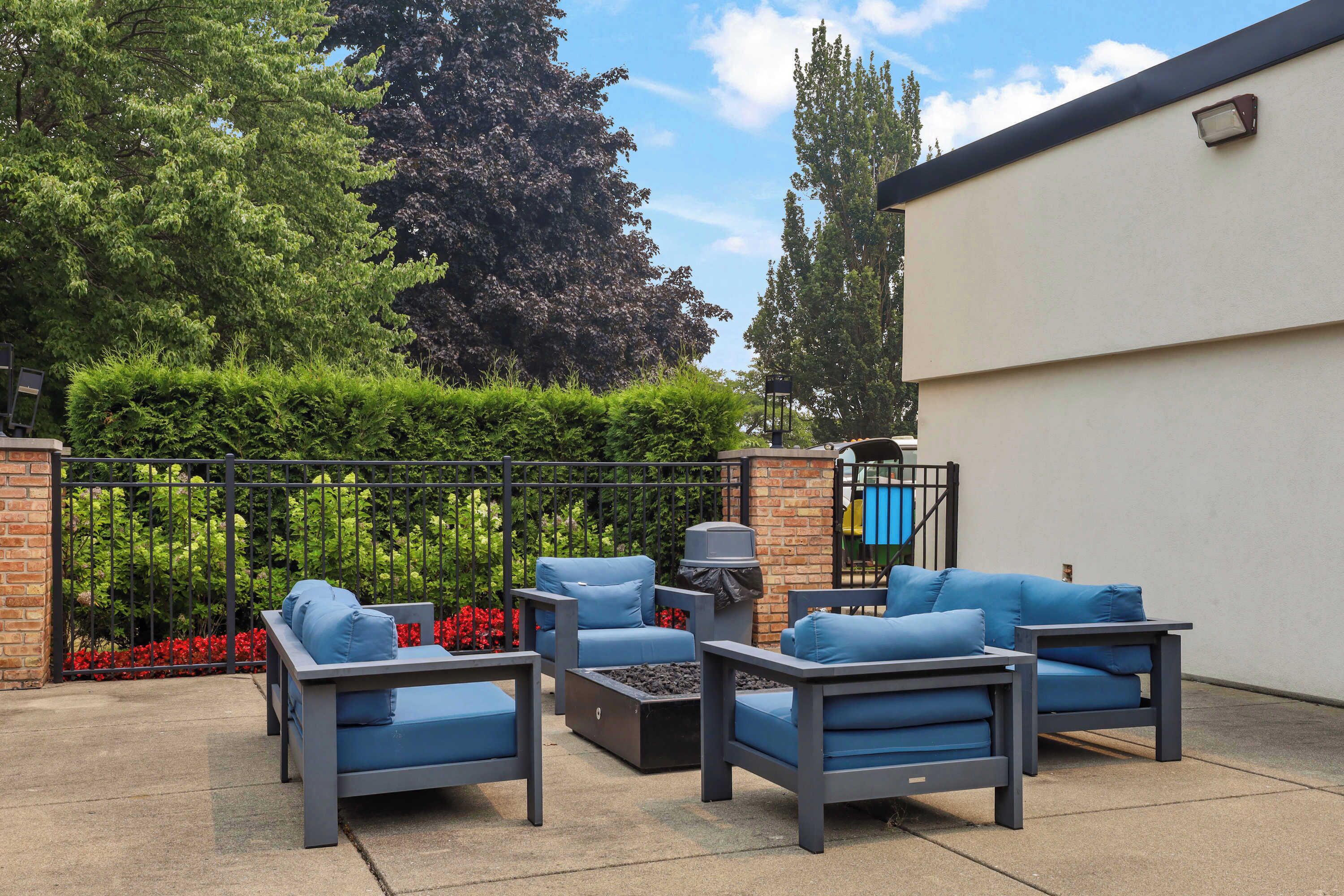 An outdoor seating area with a metal fence, a brick wall, and a white building in the background.