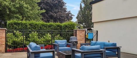 An outdoor seating area with a metal fence, a brick wall, and a white building in the background.