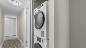 Lavandería con lavadora y secadora apiladas, una puerta que da a un pasillo y piso estampado.