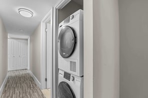 A laundry room with a stacked washer and dryer, a door leading to a hallway, and a patterned floor. - Stunning Stay in Rochester Hills (Rochester Hills)