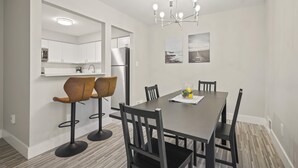 A modern kitchen with white cabinets, a stainless steel refrigerator, and a bar area with two stools. - Modern Comfort in Rochester, Perfect Getaway (Rochester Hills)