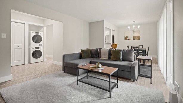 A modern living room with a grey sofa, a coffee table, and a washing machine in the background. - Modern Comfort in Rochester, Perfect Getaway (Rochester Hills)