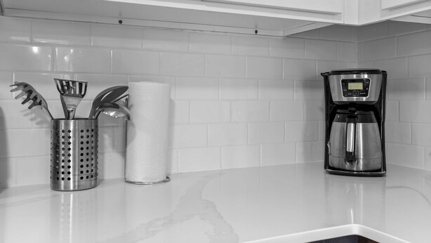 A kitchen with white cabinets, a stainless steel coffee maker, and a utensil holder with a roll of paper towels. - Getaway in the Heart of the City! (Rochester Hills)