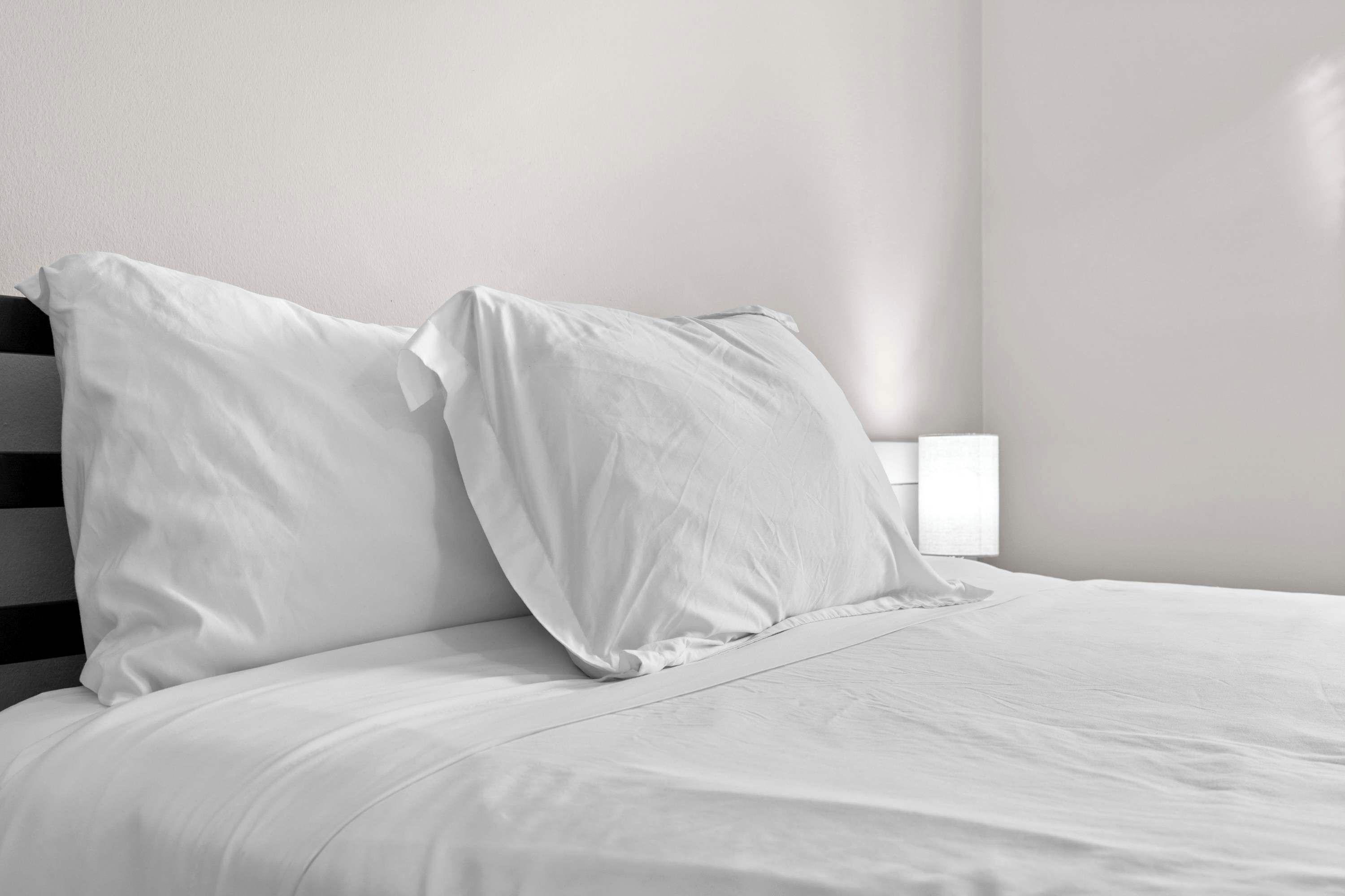 A bed with white bedding and pillows, a black headboard, and a bedside table with a white lamp.
