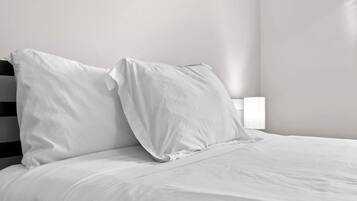 A bed with white bedding and pillows, a black headboard, and a bedside table with a white lamp.