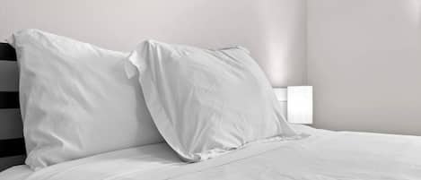Een bed met witte beddengoed en kussens, een zwart hoofdeinde en een nachtkastje met een witte lamp.