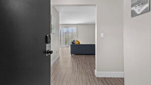 A hallway leading to a living area with a grey sofa and a window with blinds. - Getaway in the Heart of the City! (Rochester Hills)
