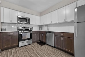 A modern kitchen with white cabinets, stainless steel appliances, and a patterned floor. - Getaway in the Heart of the City! (Rochester Hills)