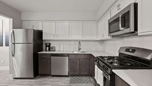 A modern kitchen with stainless steel appliances, a dishwasher, a stove, and white cabinetry. - Spacious Stay In with Great Amenities! (Rochester Hills)