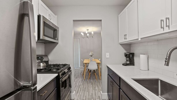 A modern kitchen with stainless steel appliances, a dining area with a chandelier, and a clean, tiled floor. - Trendy & Vibrant Unit City Experience (Rochester Hills)