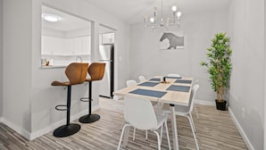 A modern kitchen with white cabinets, a stainless steel refrigerator, and a dining area with a wooden table and white chairs. - Peaceful & Trendy Unit Near Attractions (Rochester Hills)