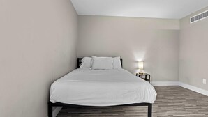 Un lit simple dans une chambre dont le plafond est en pente, avec une petite table de chevet sur laquelle se trouve une lampe.