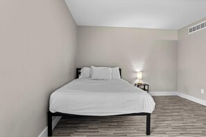 A single bed in a room with a sloped ceiling and a small bedside table with a lamp. - The Best Stay with Parking and Amenities! (Rochester Hills)