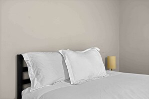 A bed with white bedding and two pillows, a bedside lamp, and a plain wall. - The Best Stay with Parking and Amenities! (Rochester Hills)
