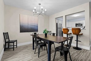 Un'area pranzo moderna con un tavolo in legno, sedie nere, una pianta in vaso e un grande quadro astratto appeso alla parete.