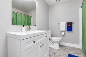 Une salle de bain avec un meuble-lavabo blanc, des toilettes et un rideau de douche vert.