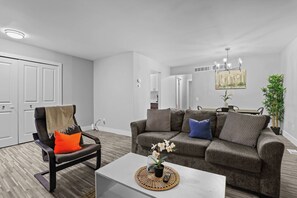 A modern living room with a sofa, armchair, and coffee table. There is a painting on the wall and a plant on the side. - Comfortable Stay near Downtown with Ammenities! (Rochester Hills)