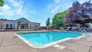 A swimming pool with lounge chairs and umbrellas, surrounded by trees and a building with large windows. - Modern 2BR Retreat w/Pool & Gym | Near Downtown (Rochester Hills)