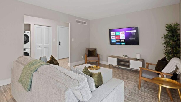 A modern living room with a grey sofa, a coffee table, and a TV mounted on the wall displaying various streaming services. - Modern 2BR Retreat w/Pool & Gym | Near Downtown (Rochester Hills)