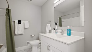 A modern bathroom with a white sink, two towel racks, a toilet, and a shower curtain. - Serene & Modern Haven for Relaxation (Rochester Hills)