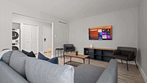 A modern living room with a grey sofa, a coffee table, and a flat-screen TV mounted on the wall displaying various streaming services. - Peaceful Rochester Escape Perfect for Families (Rochester Hills)
