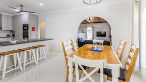 A modern kitchen with white cabinets, a black countertop, and a wooden dining table with white chairs. - Take a dip at Eucalypt (BELLARA)