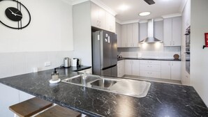 A modern kitchen with a stainless steel refrigerator, white cabinets, a black marble countertop, and a built-in oven. - Take a dip at Eucalypt (BELLARA)
