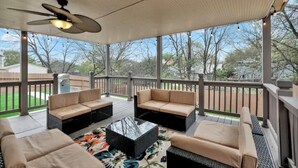 Un patio techado al aire libre con muebles de mimbre, un ventilador de techo y vista al jardín trasero.