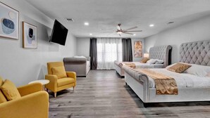 Una habitación de hotel moderna con una cama grande, un sofá, una silla, un televisor y un ventilador de techo.