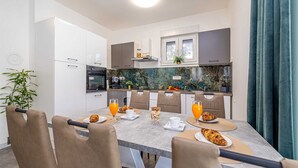 A modern kitchen with white cabinets, a built-in oven, and a dining area with a table set for breakfast. - Holiday house ASLAN with pool (Žestilac)