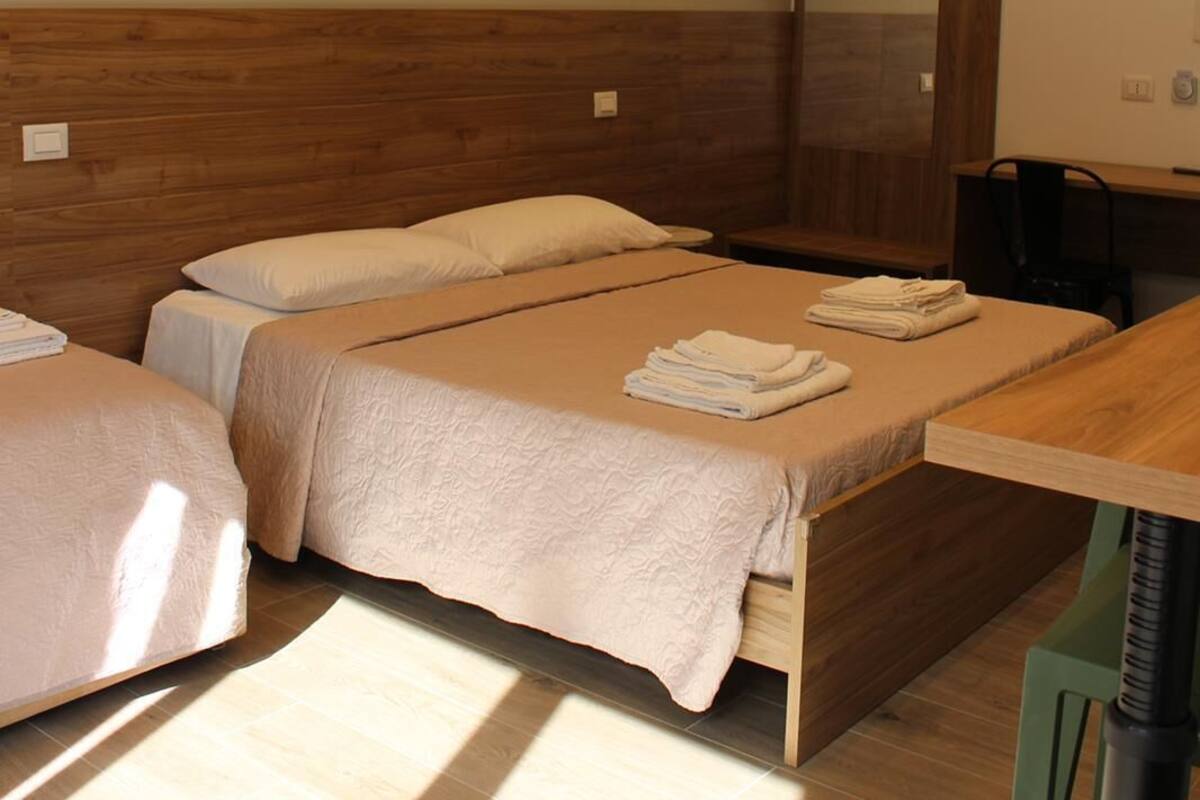 A hotel room with two beds, a wooden headboard, a mirror, a table, and a chair.