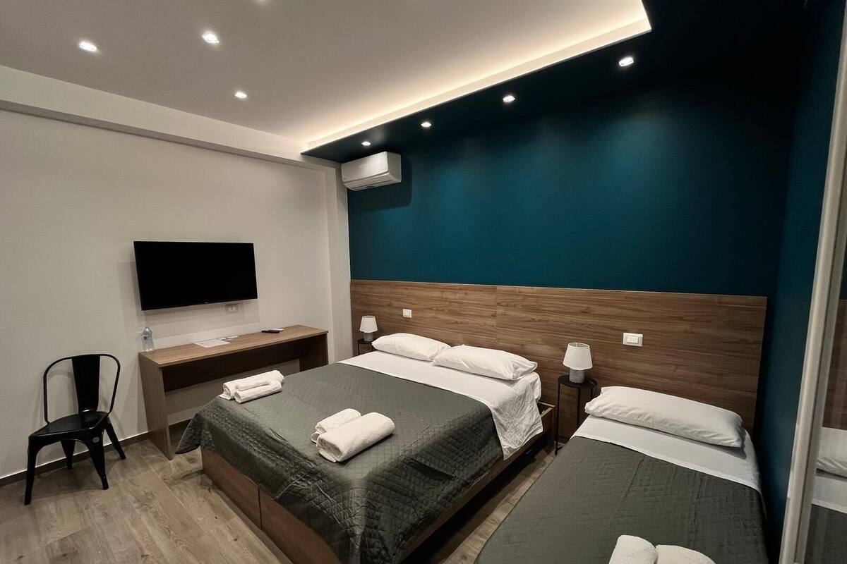 A hotel room with two beds, a desk, a chair, a TV, and an air conditioning unit.