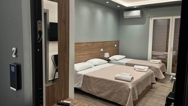 Una moderna camera d'albergo con due letti, una testiera in legno, un comodino e una televisione a parete, oltre a un condizionatore d'aria.