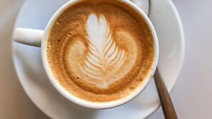 Una tazza di caffè con decorazione in schiuma di latte, un croissant su un piatto e un bicchiere di zucchero.