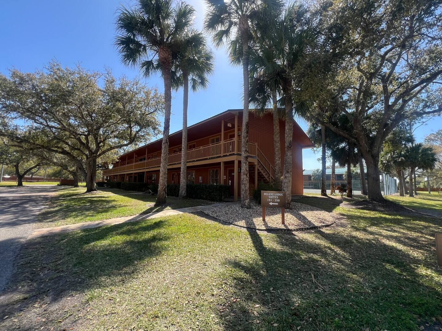 A two-story building with a balcony, surrounded by palm trees and a grassy area.