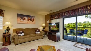 A living room with a sofa, a coffee table, a television, and a balcony with outdoor furniture. - Walk-in condo with Golf Course View Near the Strip. NO STAIRS! (Branson)