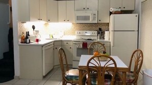A compact kitchen with white cabinets, a microwave, a stove, and a refrigerator. There is a dining table with chairs and a small island with a sink.
