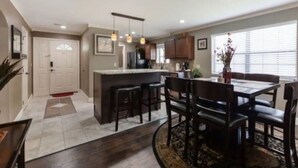 A modern kitchen with a central island, dark wooden dining table, and pendant lighting.