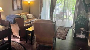 A living room with a sofa, chairs, a table, and a large window with curtains.