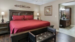 A bedroom with a large bed, two bedside tables, a bench, a dresser, and a mirror.