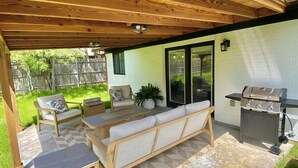 An outdoor patio with wooden furniture, a grill, and a covered area with a view of the backyard.