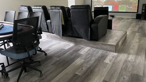 Une salle de conférence dotée d’un grand écran, de fauteuils en cuir, d’un bureau avec un ordinateur portable et d’un plancher en bois.