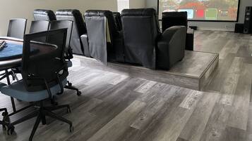A conference room with a large screen, leather chairs, a desk with a laptop, and a wooden floor.